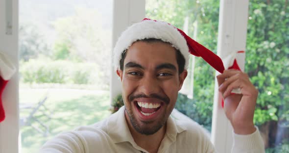 Portrait of cheerful biracial young man in santa hat gesturing during christmas video call