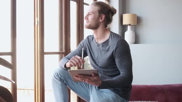 Man holds a digital tablet and looks out of the window