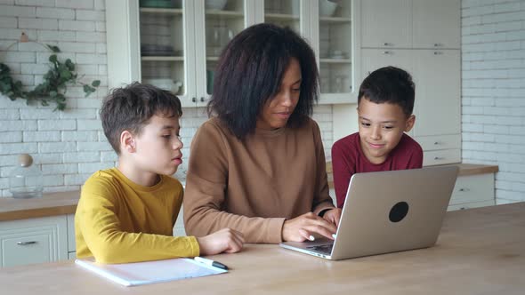 Smiling African American Mother and Kids Sons Having Fun with Computer Sitting at the Kitchen Table