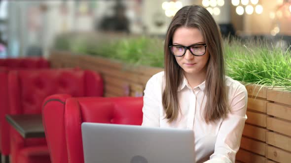 Portrait of Smiling Pensive Young Businesswoman Wearing Glasses Using Laptop