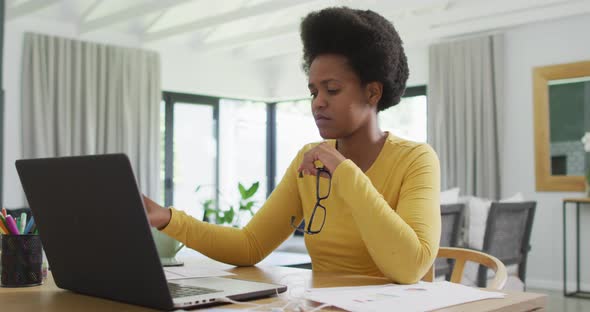 Tired african american woman sitting at table using laptop
