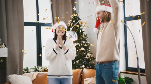 Multiracial Couple Laughing and Throwing Up Golden Confetti Fooling Around at Home Against Decorated