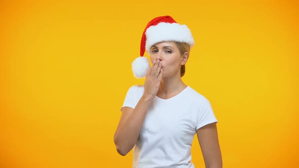 Pretty Woman in Santa Hat Sending Air Kiss on Bright Background, Flirt Gesture