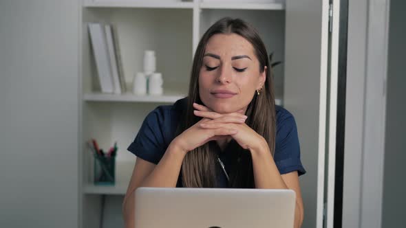 Attractive Femake Doctor Practitioner in Darkblue Coat Sitting at Workplace Thinking of Problem