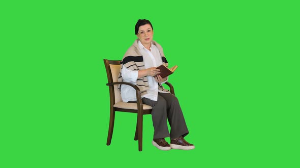 Happy Senior Woman Reading a Book Aloud on Camera on a Green Screen Chroma Key