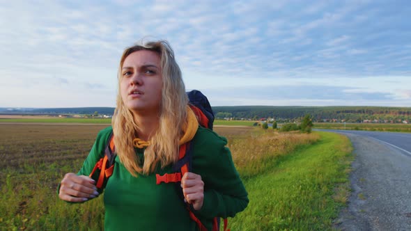 Girl Traveller with Backpack is Walking Along the Road