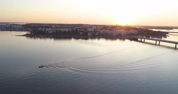 Wide aerial shot that circles around the subject and reveals the sunset and archipelago while contin