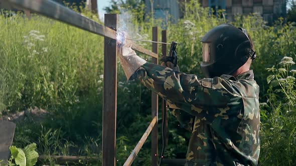 Slow Motion Side View Handyman in Mask Welds Metal Fence