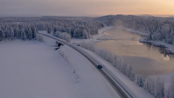 Aerial view orbits freezing Scandinavia woodland lake crossing following vehicle on journey through