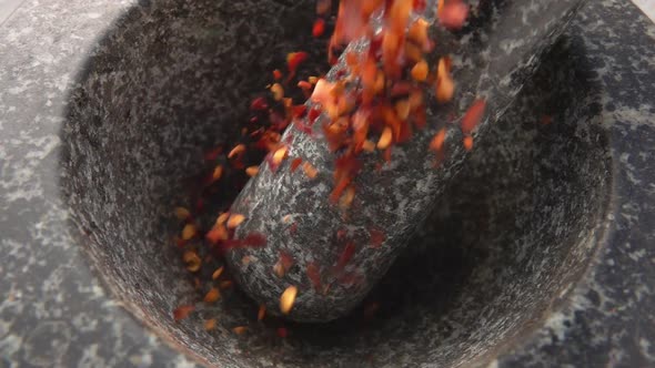 Pieces of Red Hot Chilli Pepper Are Falling Into the Stone Mortar