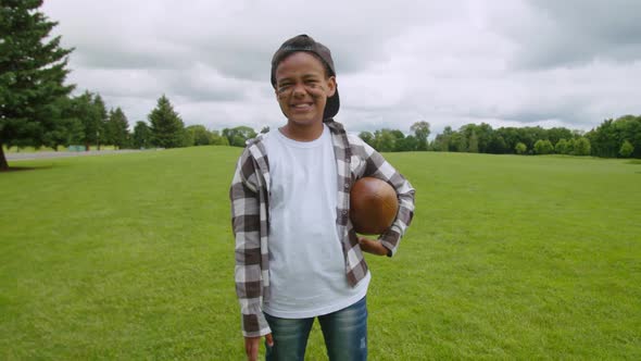 Positive Little African Boy with American Football Ball Posing Outdoors