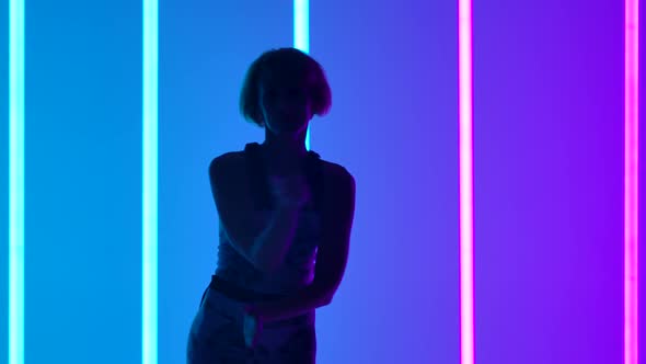 Silhouette of a Young Stylish Girl Dancing on the Background of Multicolored Neon Tubes