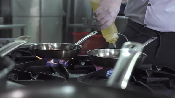 Chef Pours Fresh Oil Onto Frying Pans on Contemporary Stove