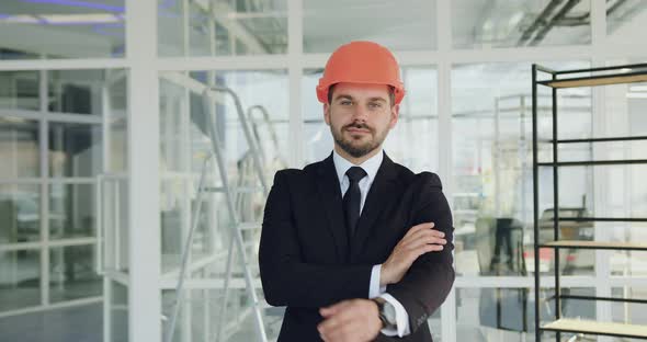 Engineer in Hardhat Poses on Camera with Crossed Arms in Unfinished Office Building