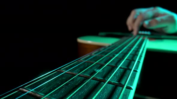Man Musician Plays a Wooden Acoustic Guitar on a Black Background with Green Light