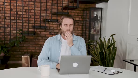 A Man at His Desk Yawns While Sitting at a Computer