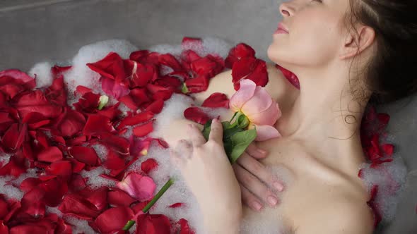 Sexy Girl Lies in a Big Stone Bath with a Rose Flower in Her Hands