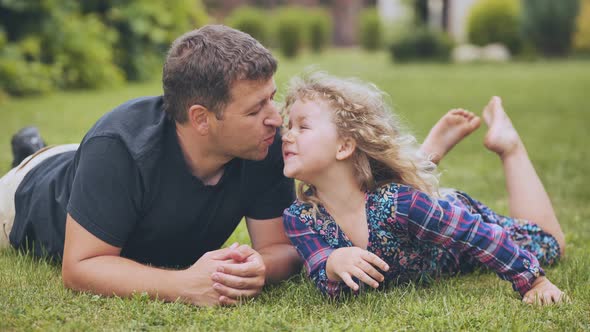 A Father Kisses His Young Daughter in the Garden While Lying on the Grass