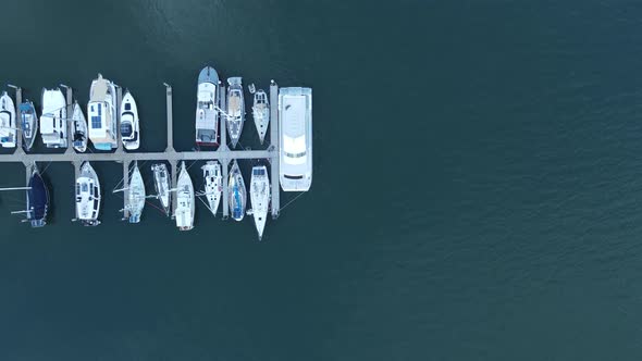 A static high drone view looking down at multiple boats docked on a wharf in a protected harbor loca