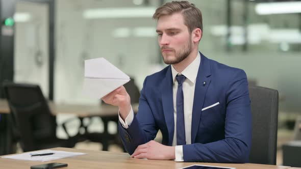 Pensive Businessman Holding Paper Plane at Work