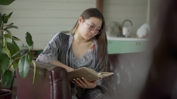 Intelligent Beautiful Asian Woman in Eyeglasses Looking Through Notes in Workbook in Home Office