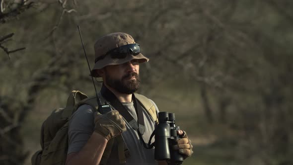 Outdoor Shot of Serious Bearded Man Hunter or Guard in Military Tshirt and Hat Holding Backpack with