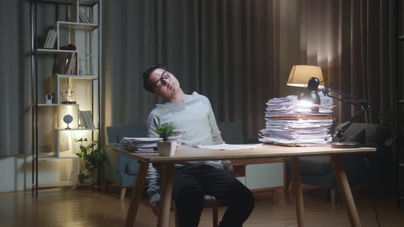 Tired Asian Man Leaning On The Home Chair And Sleeping While Working Hard With Documents