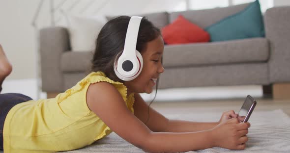 Happy hispanic girl watching video on tablet wearing head phones lying on floor
