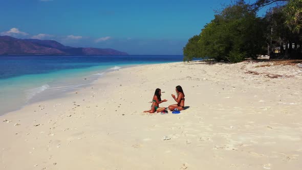 Female models enjoying life on luxury coast beach holiday by blue ocean with bright sandy background