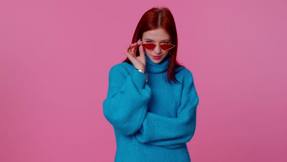 Seductive Cheerful Redhead Girl in Blue Sweater Wearing Sunglasses Charming Smile on Pink Wall