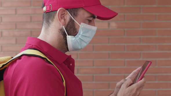 Delivery Young Man in Protective Man Wearing Red Uniform Using Smart Phone