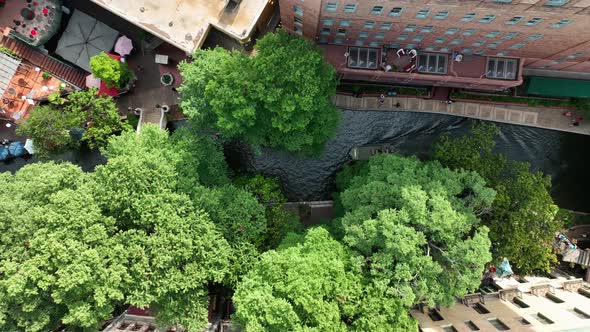 Top down aerial of San Antonio River Walk. Boats navigate waterway in downtown urban park.