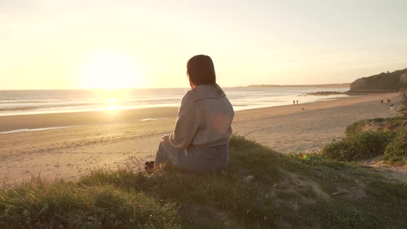 Traveling woman sitting on hill against sunset sky near sea