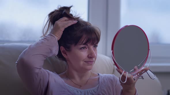 Happy Woman Sits on the Sofa and Looks in the Mirror Admires