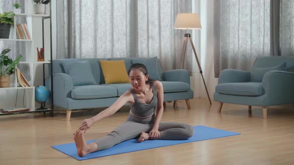 Asian Athletic Female In Sports Clothes Sitting On A Yoga Mat And Doing Hamstring Stretch At Home