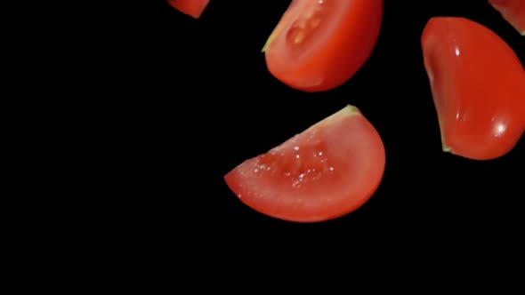 Delicious Small Red Cut Tomato Slices Fall Diagonally on a Black Background