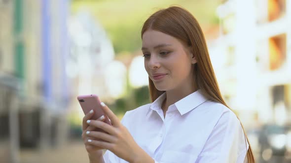 Cheerful Caucasian Girl Messaging on Smartphone Outdoor and Smiling, Application