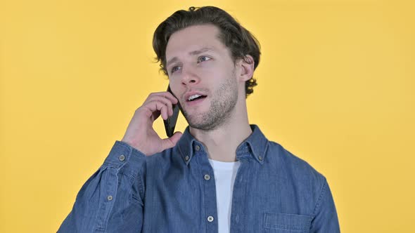 Portrait of Young Man Talking on Smartphone on Yellow Background