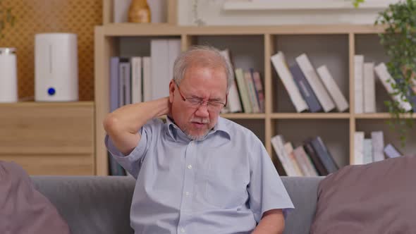 Asian Older man suffering from shoulders and neck pain sitting on sofa. Health problem retired Asian