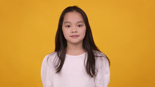 Studio Portrait of Cute Asian Girl Looking at Camera Orange Background