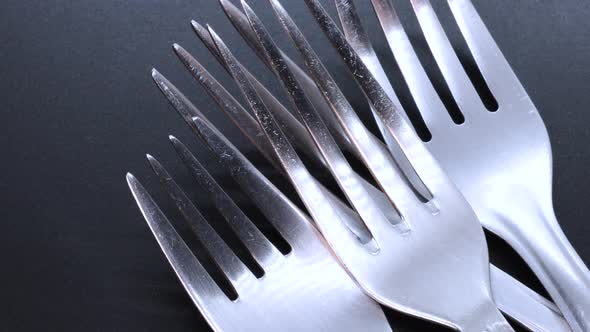 Macro shot of four steel forks on a black bacground, rotating motion. Close up view from above.