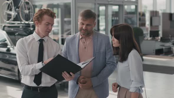 Salesman with Folder Talking to Couple in Dealership