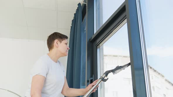 Senior Woman Cleaning Window at Home with a Vacuum Cleaner