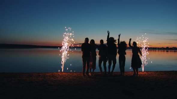 Joyful Young People Dancing Jumping on Beach Enjoying Fireworks and Fun Late at Night