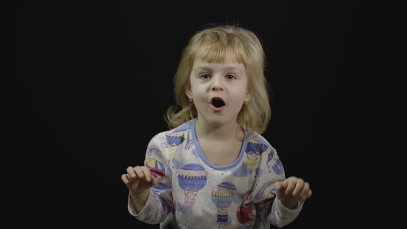 Little Baby Girl in Pajama Is Fooling Around and Make Faces. Black Background