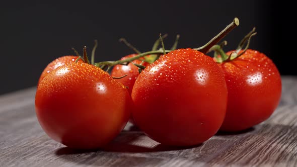 Appetizing Red Juicy Tomatoes on a Branch with Water Drops Lie on a Wooden Surface and Spin