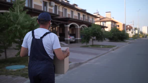 Delivery Man Walking Along Townhouses with Box