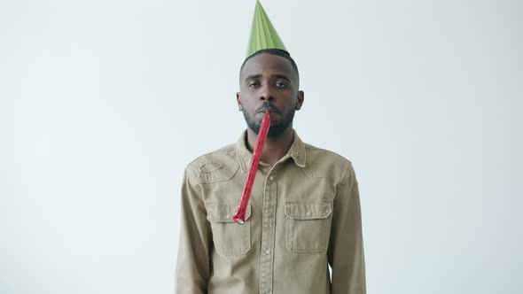Slow Motion Portrait of African American Man Wearing Bright Hat Blowing Party Horn with Miserable