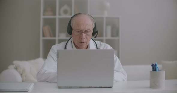 Male Doctor Is Consulting Online Colleagues and Patients, Elderly Male Therapist Is Sitting at