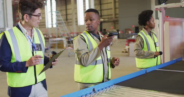 Diverse male and female workers talking next to conveyor belt in warehouse